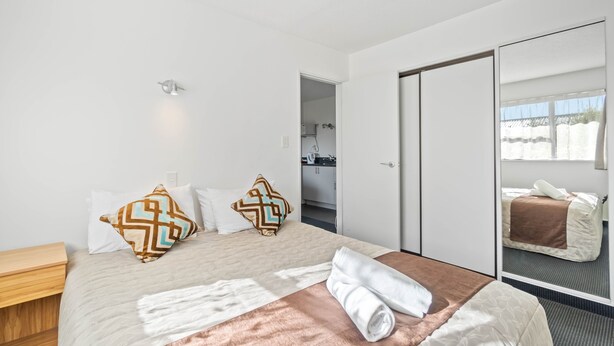 A modern hotel room with a large bed, a wooden nightstand, a mirror, and a view of the outside. - Ascot Vale Motor Lodge (Christchurch)