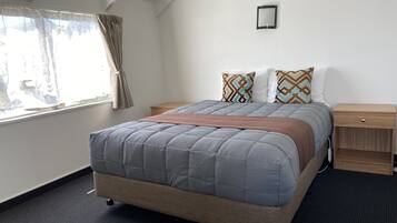 Quarto bem arrumado com cama, mesas de cabeceira, janela com cortinas e luminária na parede.