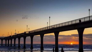 A pier extending over the water with people walking on the beach below. - Ascot Vale Motor Lodge (Christchurch)