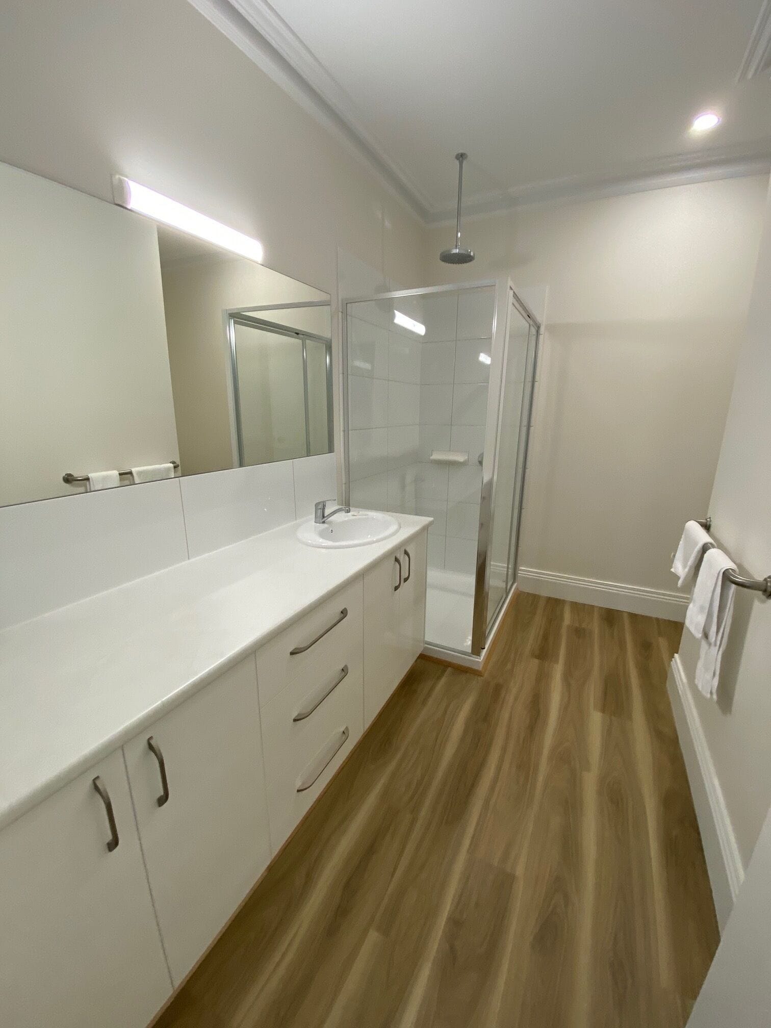 A modern bathroom with a white vanity, a glass shower enclosure, and a wooden floor.