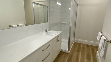 A modern bathroom with a white vanity, a glass shower enclosure, and a wooden floor.