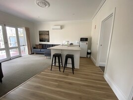 A modern kitchen with a central island, two stools, a refrigerator, and a microwave.