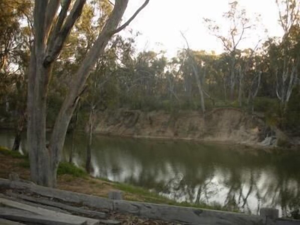 A natural landscape with a body of water, trees, and a wooden fence. - Campaspe Lodge Echuca (Echuca)