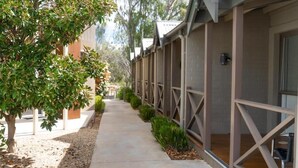 A corridor with a covered walkway, trees, and a building with a brick facade and metal railings. - Campaspe Lodge Echuca (Echuca)