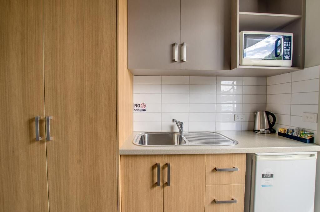 A compact kitchen with wooden cabinets, a stainless steel sink, and a microwave on the countertop.