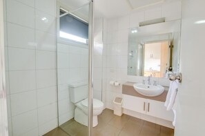 Een moderne badkamer met een douchecabine van glas, een wit toilet, een wastafel met spiegel erboven en een handdoekrek.