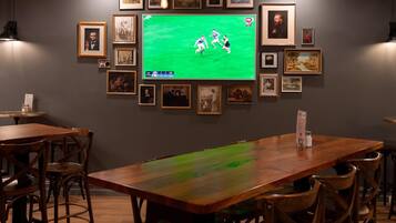Quarto com uma televisão grande exibindo um jogo esportivo, obras de arte nas paredes e mobiliário de madeira.