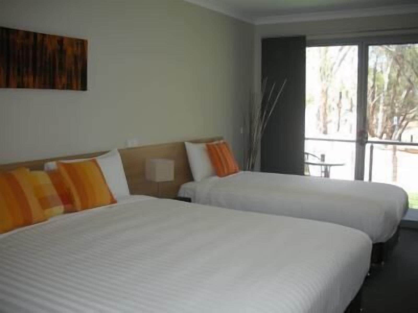 Habitación de hotel con dos camas, un ventanal grande y vistas a árboles.