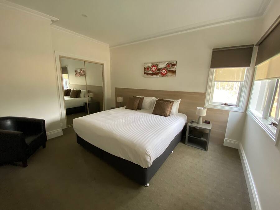 A hotel room with a large bed, a bedside table with a lamp, a chair, and a window with blinds.