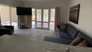 A modern living room with a grey sofa, a flat-screen TV mounted on the wall, and a sliding glass door leading to an outdoor deck. - Campaspe Lodge Echuca (Echuca)