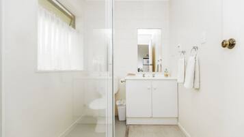 A modern bathroom with a glass shower enclosure, a white sink with a mirror above it, and a toilet.