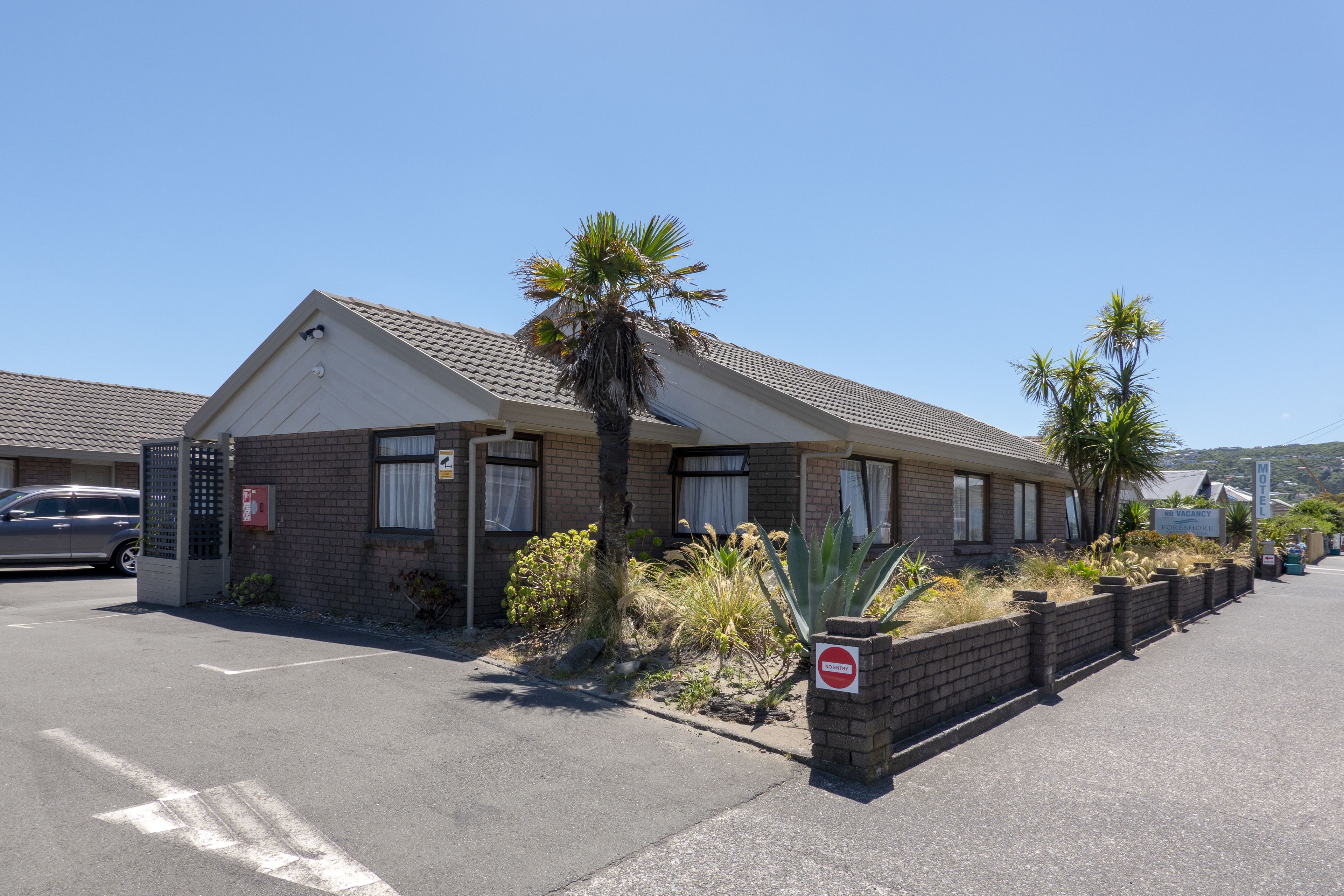 A motel with a brick facade, palm trees, and a 'No Parking' sign.