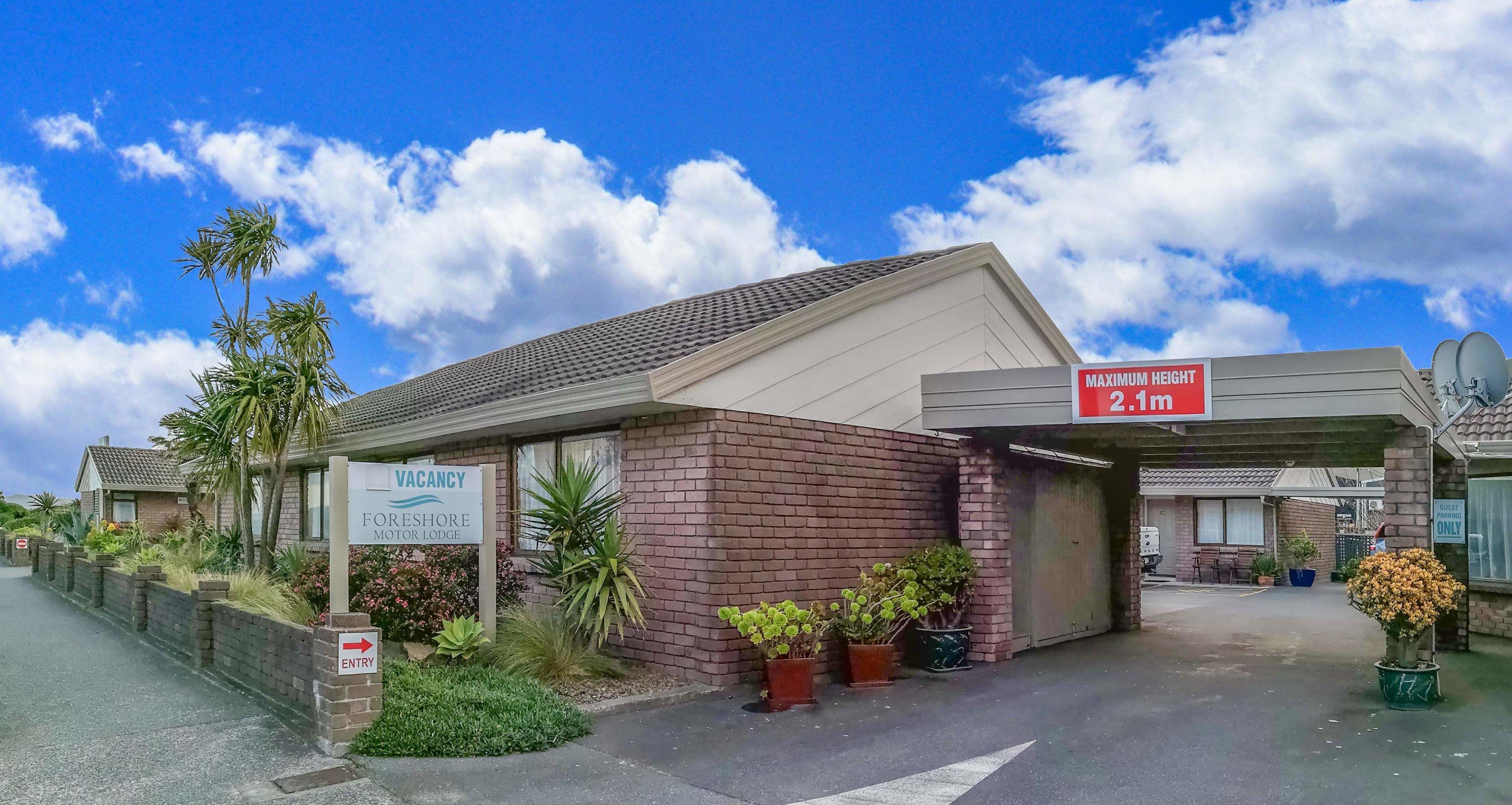Un motel con un letrero de 'VACANCY', un letrero que indica 'ALTURA MÁXIMA 2.1m' y un letrero que dice 'SOLO CLIENTES'.