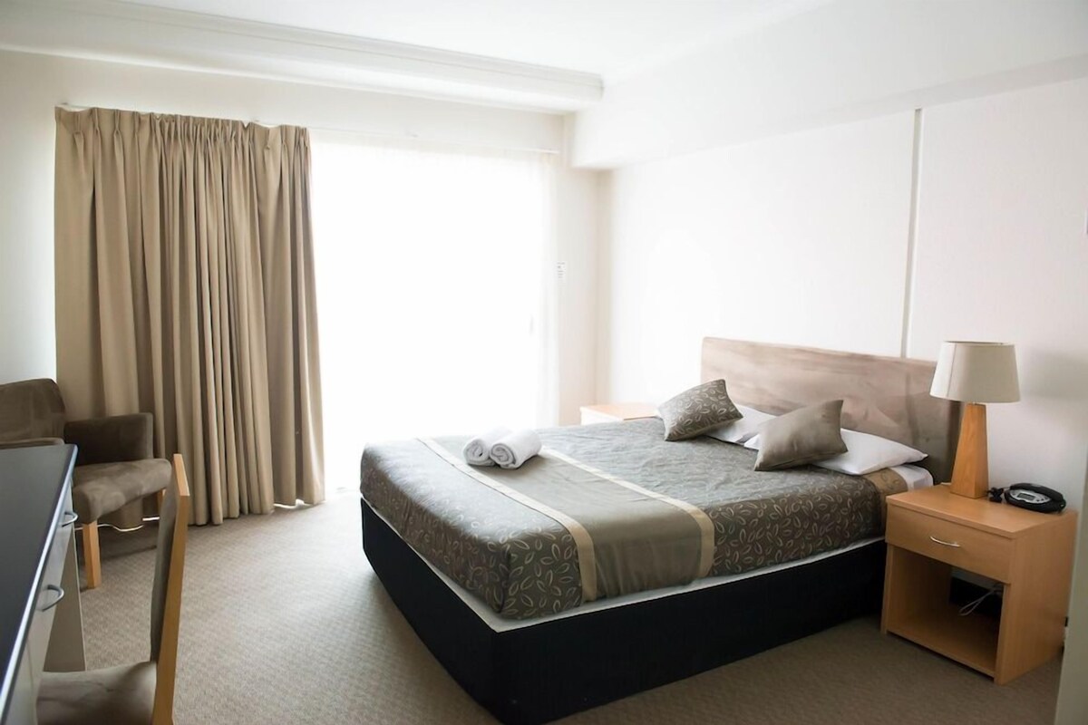 A hotel room with a bed, bedside tables, a desk, and a chair.