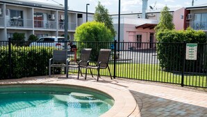 Zona de piscina con terraza de ladrillo, dos sillas de descanso y piscina cercada.
