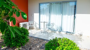 Un patio con mesa y sillas, una puerta corrediza de vidrio y un pequeño jardín con grava y plantas.