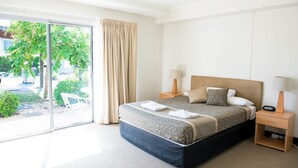 Habitación de hotel con una cama grande, dos mesitas de noche, una ventana con cortinas y vistas a zonas verdes.