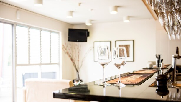 Un comedor moderno con una mesa negra, dos copas de vino y una zona de bar con copas colgando en la parte superior.