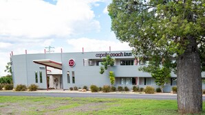 A modern building with a sign reading "Capella Coach Inn." It features a flat roof, large windows, and a well-maintained lawn in front.
