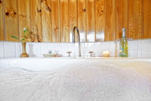 Een badkamer met een houten wand, een witte badkuip, een vaas met bloemen, een kaars en een fles lotion.