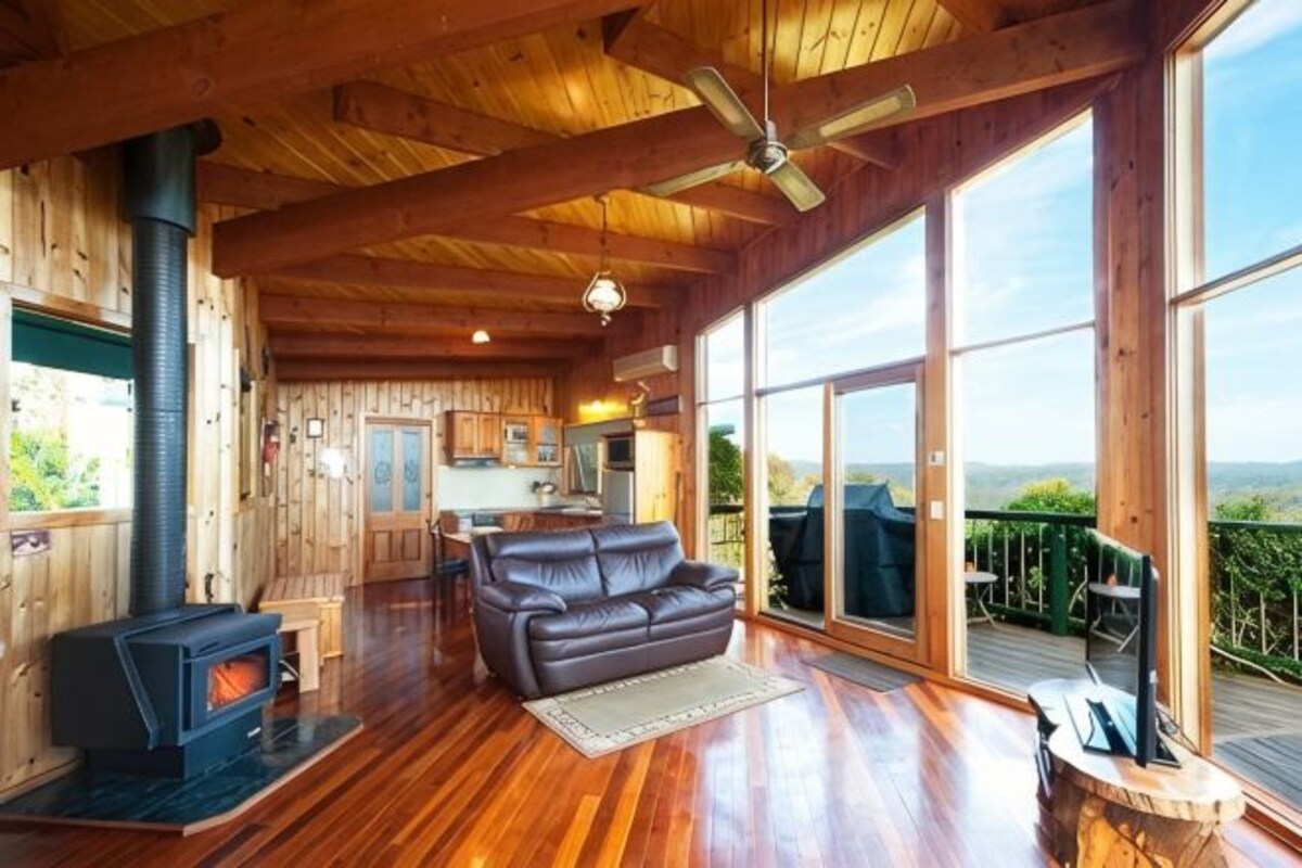 A wooden interior with a fireplace, a leather sofa, and large windows offering a view.
