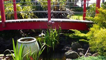 Een rode brug over een vijver met waterlelies en groene planten.