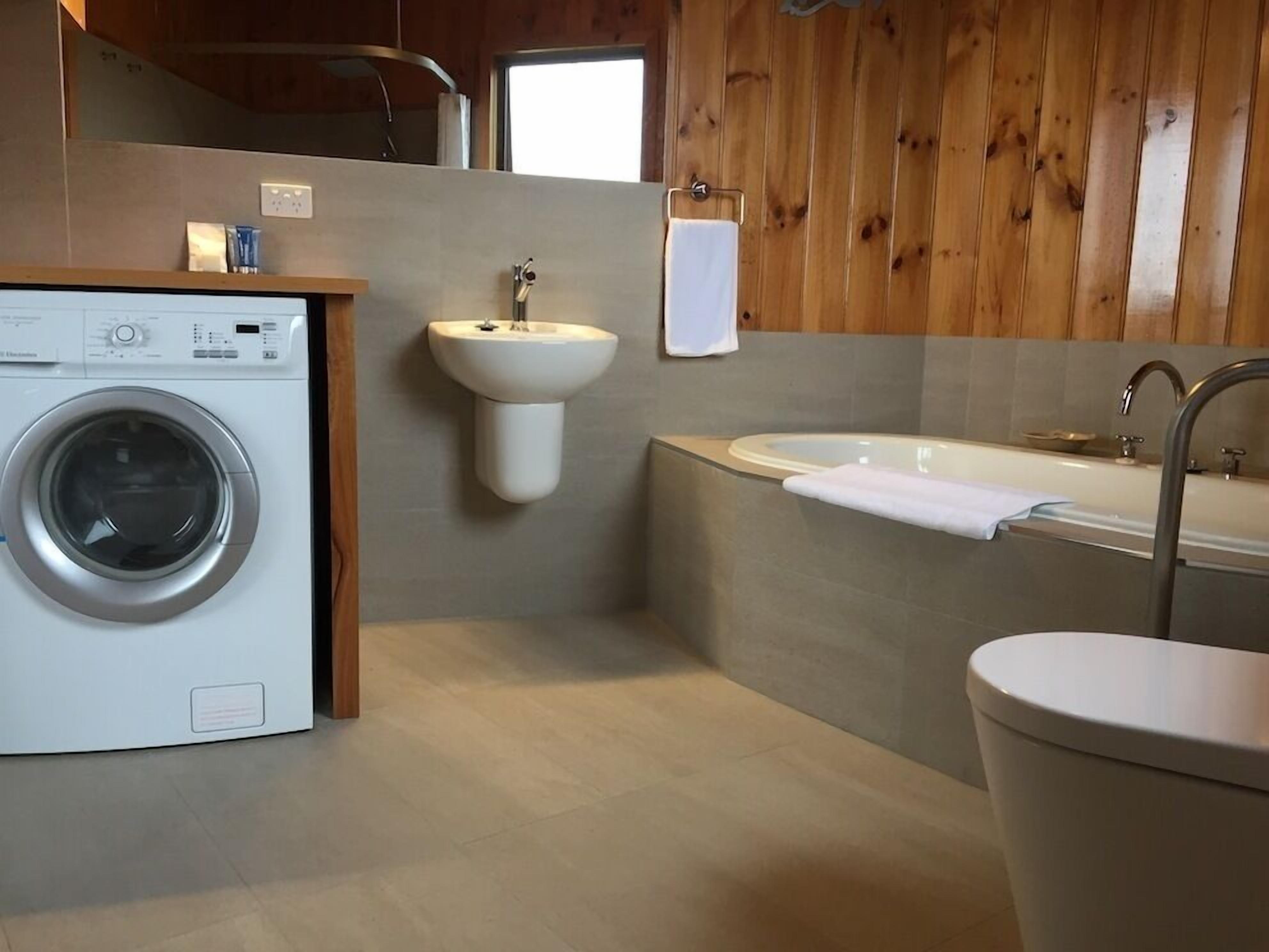 Een moderne badkamer met een wasmachine, wastafel en bad.