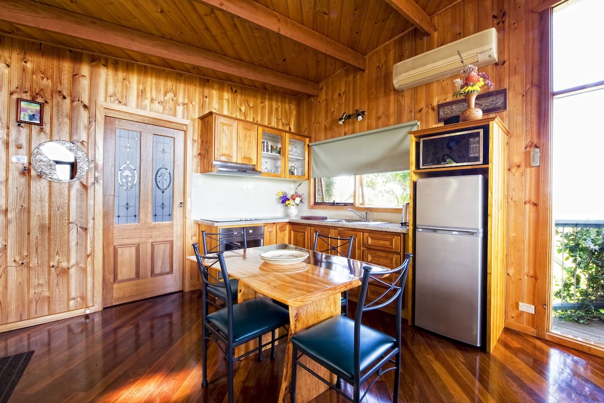 Interior em madeira com mesa de jantar, cadeiras, frigorífico e armários de madeira.