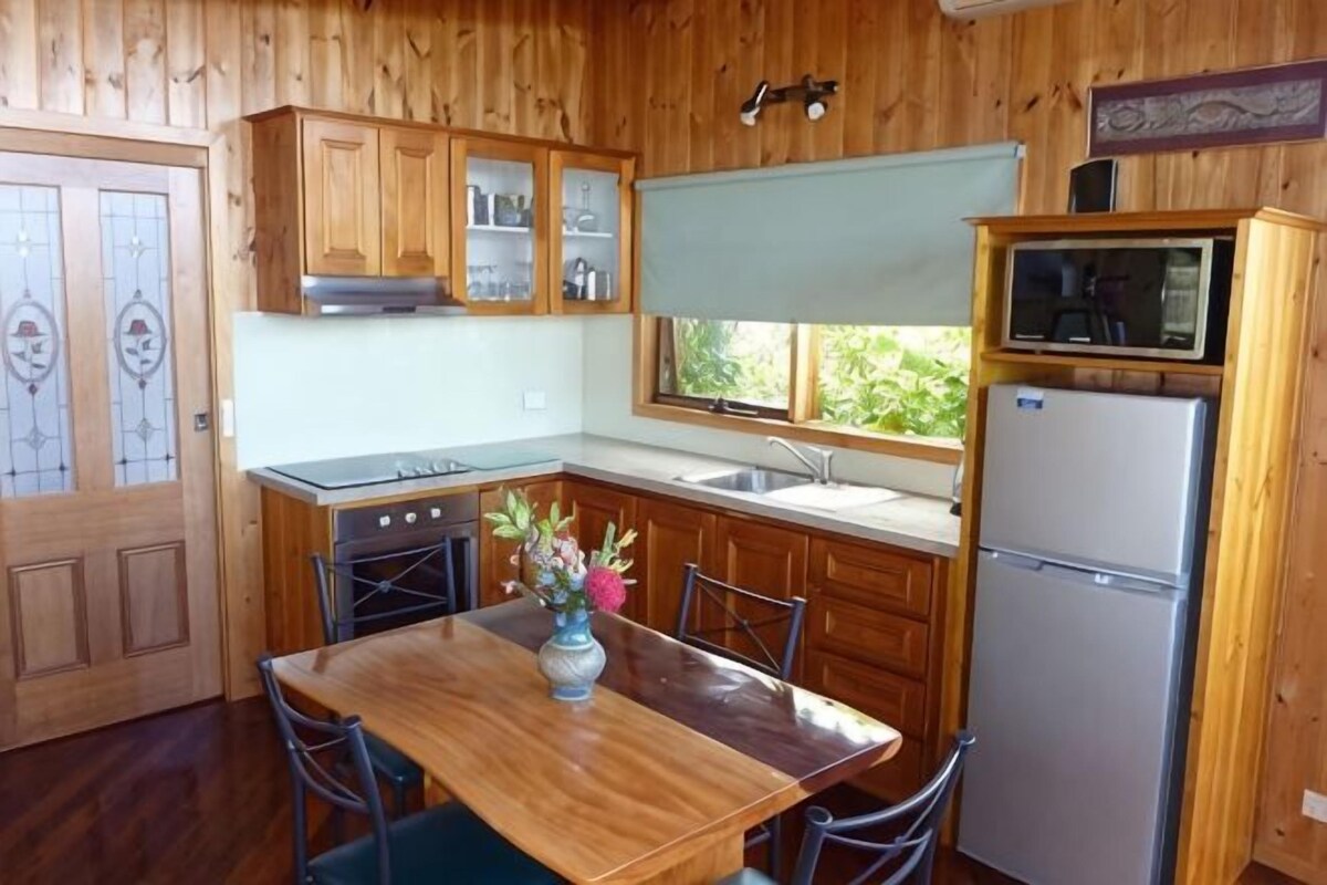 Une cuisine aux murs lambrissés, avec une table à manger, des chaises, un réfrigérateur et une fenêtre.