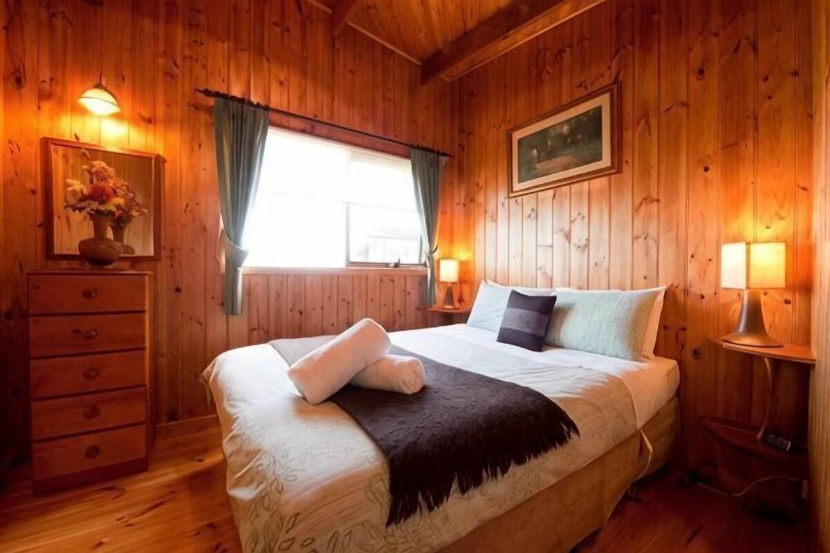 Quarto com painéis de madeira, cama, penteadeira e duas luminárias de cabeceira.