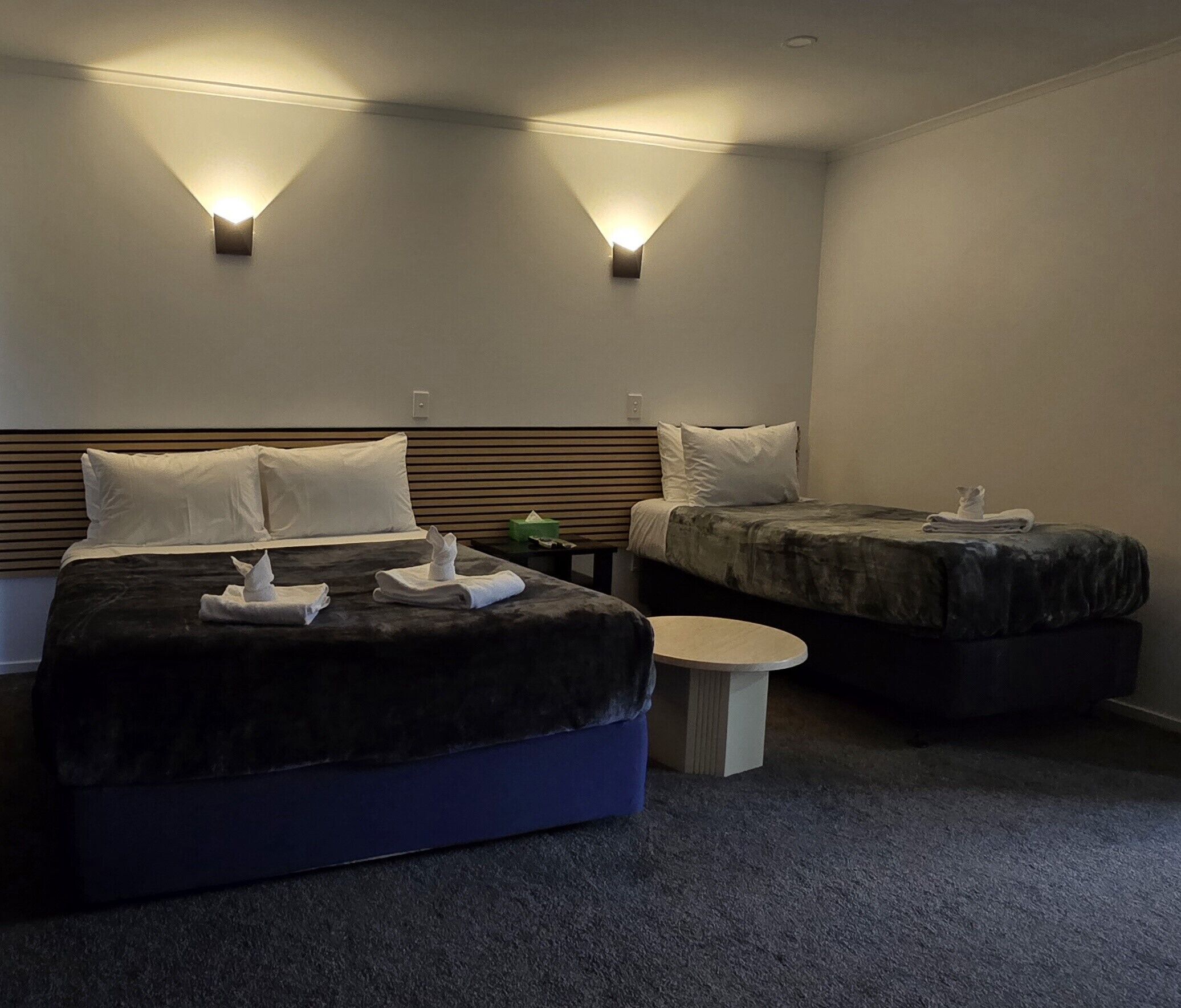A hotel room with two beds, a small round table, and two wall-mounted lights.
