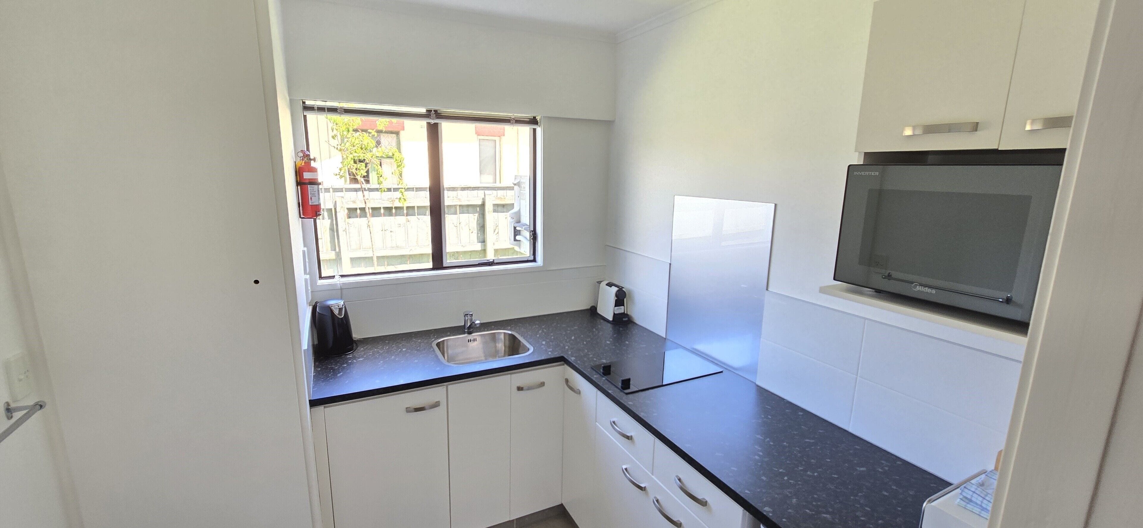 A compact kitchen with a stainless steel sink, a window with a view, white cabinets, and a built-in microwave.