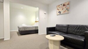 Una camera d'albergo con un divano in pelle nera, un tavolino rotondo e un letto con testiera bianca.
