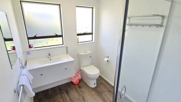A bathroom with a white sink, mirror, and toilet, wooden flooring, and a glass shower enclosure.