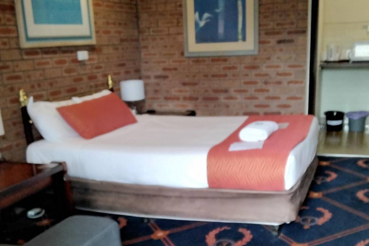 Ein Hotelzimmer mit Backsteinwand, einem Bett mit weiß-orangefarbenem Überwurf, einem Nachttisch und einer Lampe.