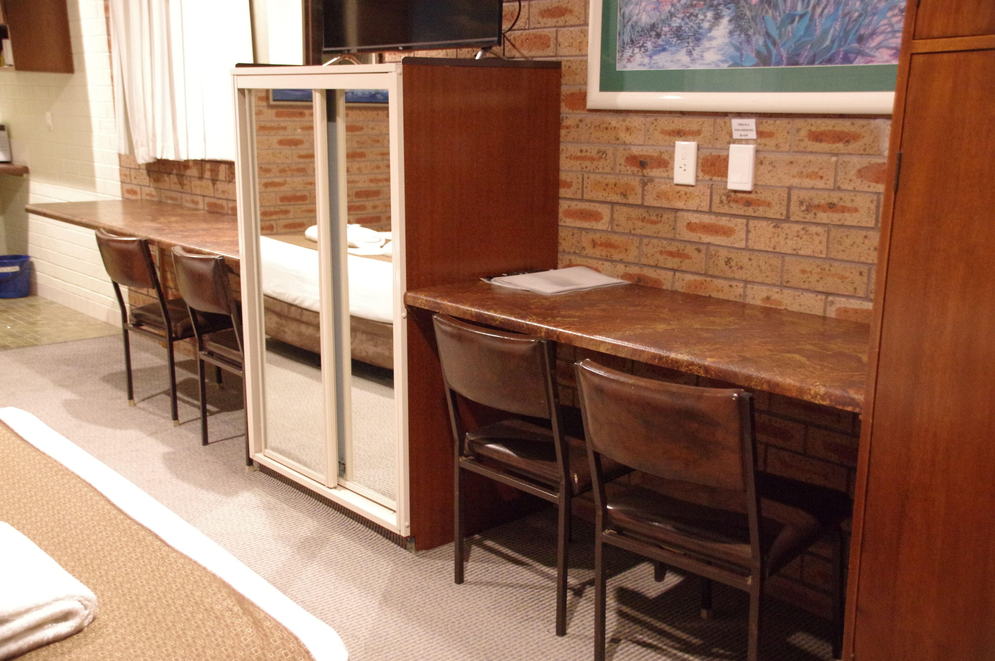 A hotel room with a brick wall, a wooden desk, and two chairs.