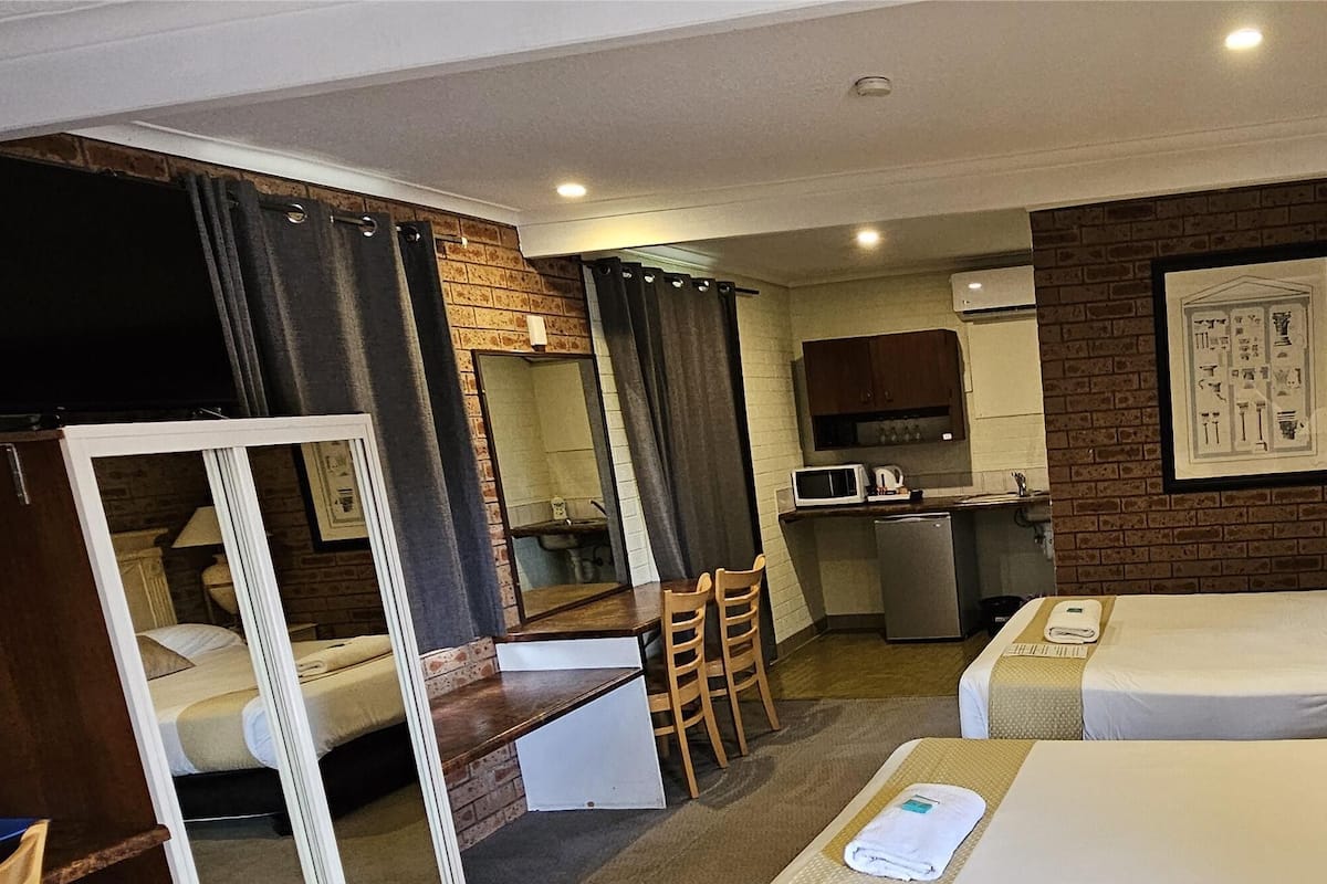 Ein Hotelzimmer mit zwei Betten, einem Schreibtisch, einem Sessel, einem Fernseher, einem Badezimmer und einer Küchenzeile.