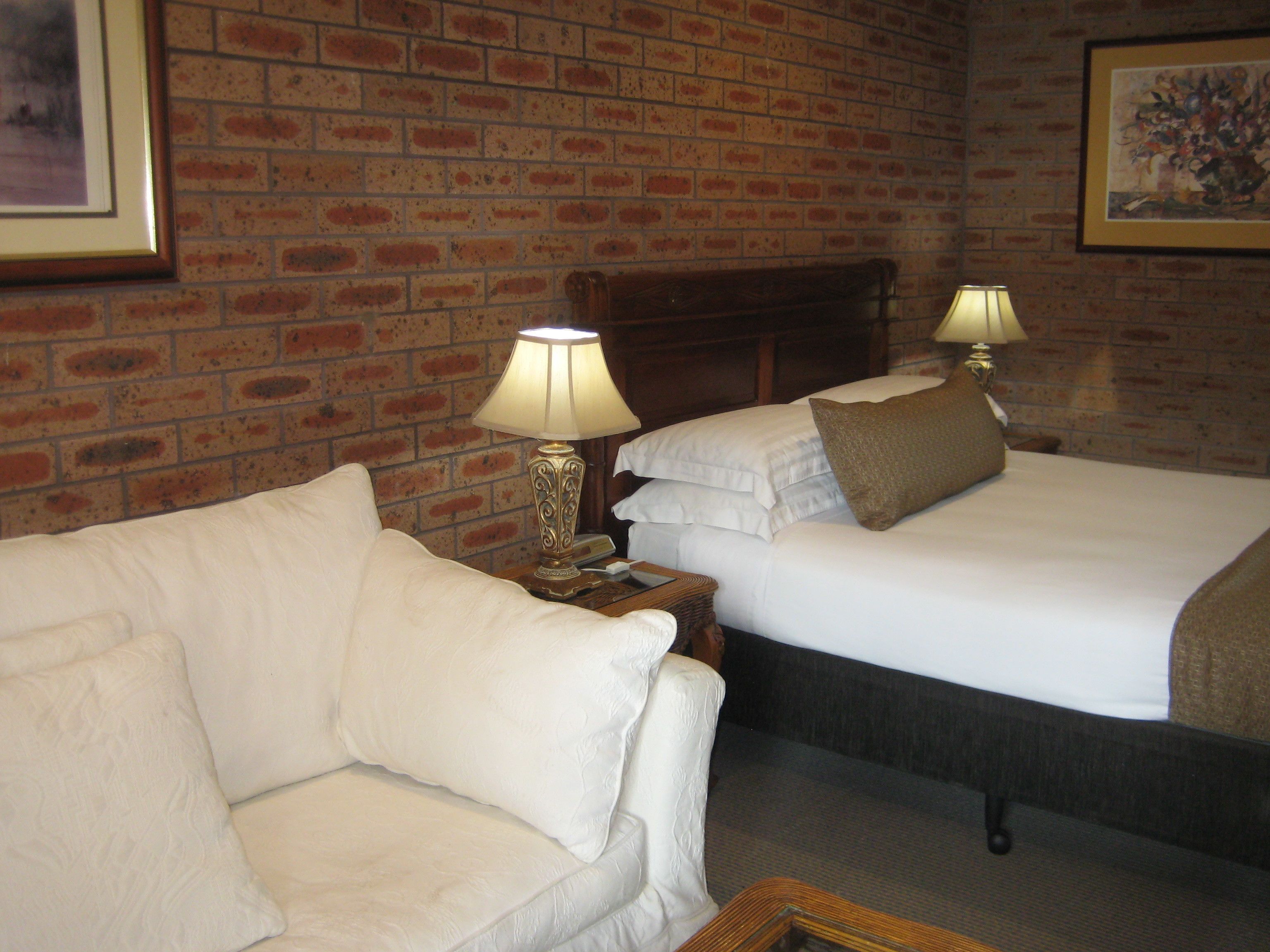 Una habitación de hotel con pared de ladrillo, sofá blanco, dos camas con ropa de cama blanca y dos lámparas de noche.
