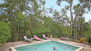 Una piscina rectangular rodeada por una valla de metal negro, con sillas de descanso y un banco a lo largo del borde.