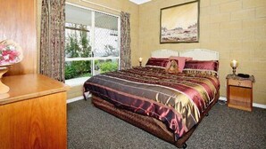 Un dormitorio con una cama grande, un aparador de madera, una mesita de noche, una ventana con cortinas y un cuadro en la pared.
