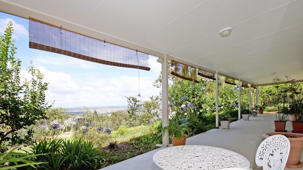 Un patio cubierto con mobiliario blanco, plantas en macetas y vistas al campo.