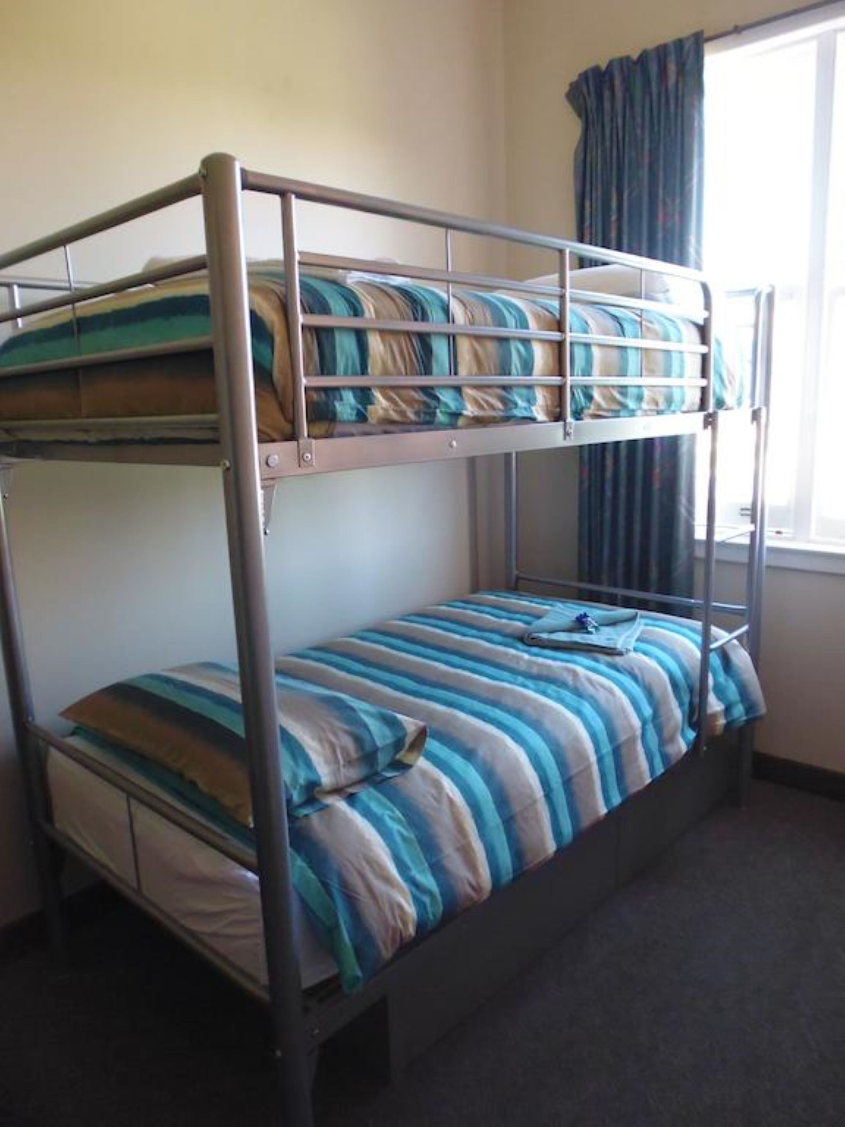 Ein Stockbett mit gestreifter Bettwäsche in einem Zimmer mit Fenster und Vorhängen.