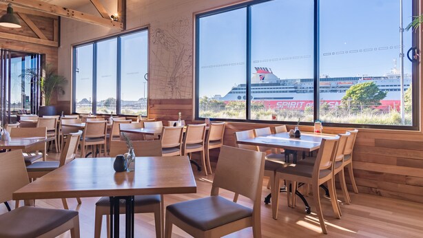 A restaurant with large windows, wooden tables, and chairs. - Formby Hotel (Devonport)