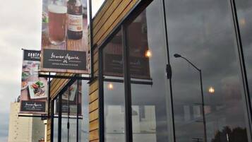 Ein Gebäude mit großen Fenstern und Holzverkleidung. Es wehen Banner, die ein Restaurant und ein Café bewerben.