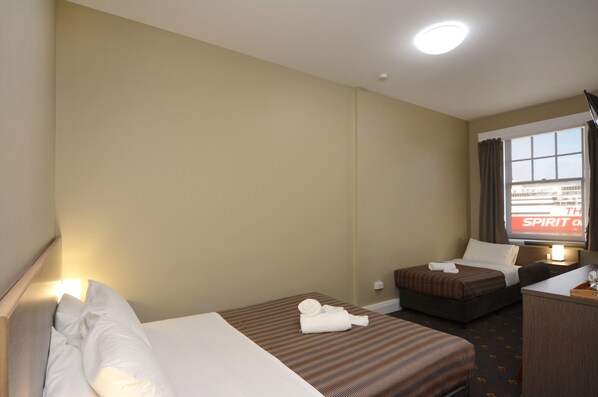 Habitación de hotel con dos camas, un escritorio, una ventana con cortinas y un televisor mostrando 'SPIRIT ON'.
