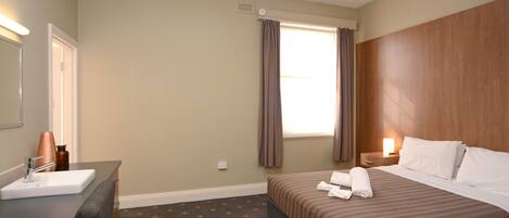 Habitación de hotel con cama, mesita de noche con lámpara, baño con lavamanos y espejo, y ventana con cortinas.