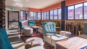A modern interior with a mix of seating options, including chairs and ottomans, arranged around tables. - Formby Hotel (Devonport)