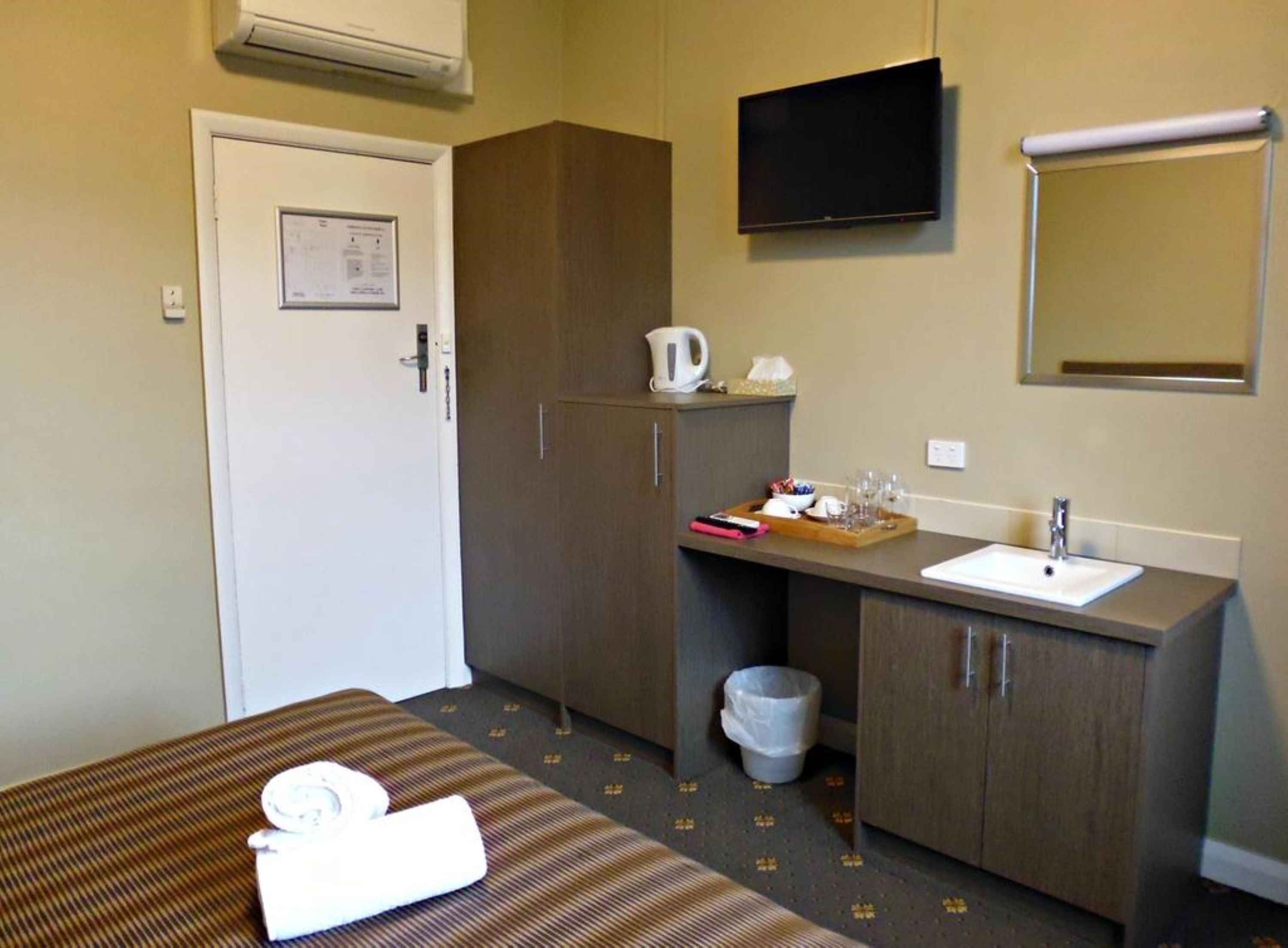 Habitació d'hotel amb un llit, una escriptori amb un rentanet, una televisió i un armari.