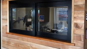 A reception area with a sign above a window, wooden paneling on the wall, and a reflection of a person inside.