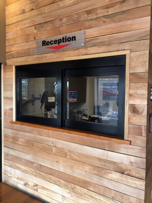 A reception area with a sign above a window, wooden paneling on the wall, and a reflection of a person inside.